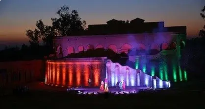 Ancient amphitheater lit with rainbow-colored lights at sunset, highlighting arches and steps.