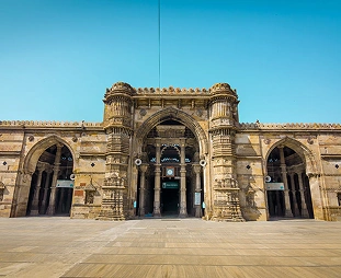 Historic stone arch gateway with a central large arch and two side arches against a clear blue sky.