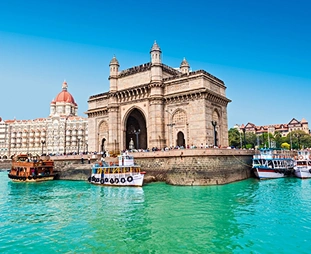Historic stone arch gateway along a harbor, with boats in turquoise water and a cityscape behind.